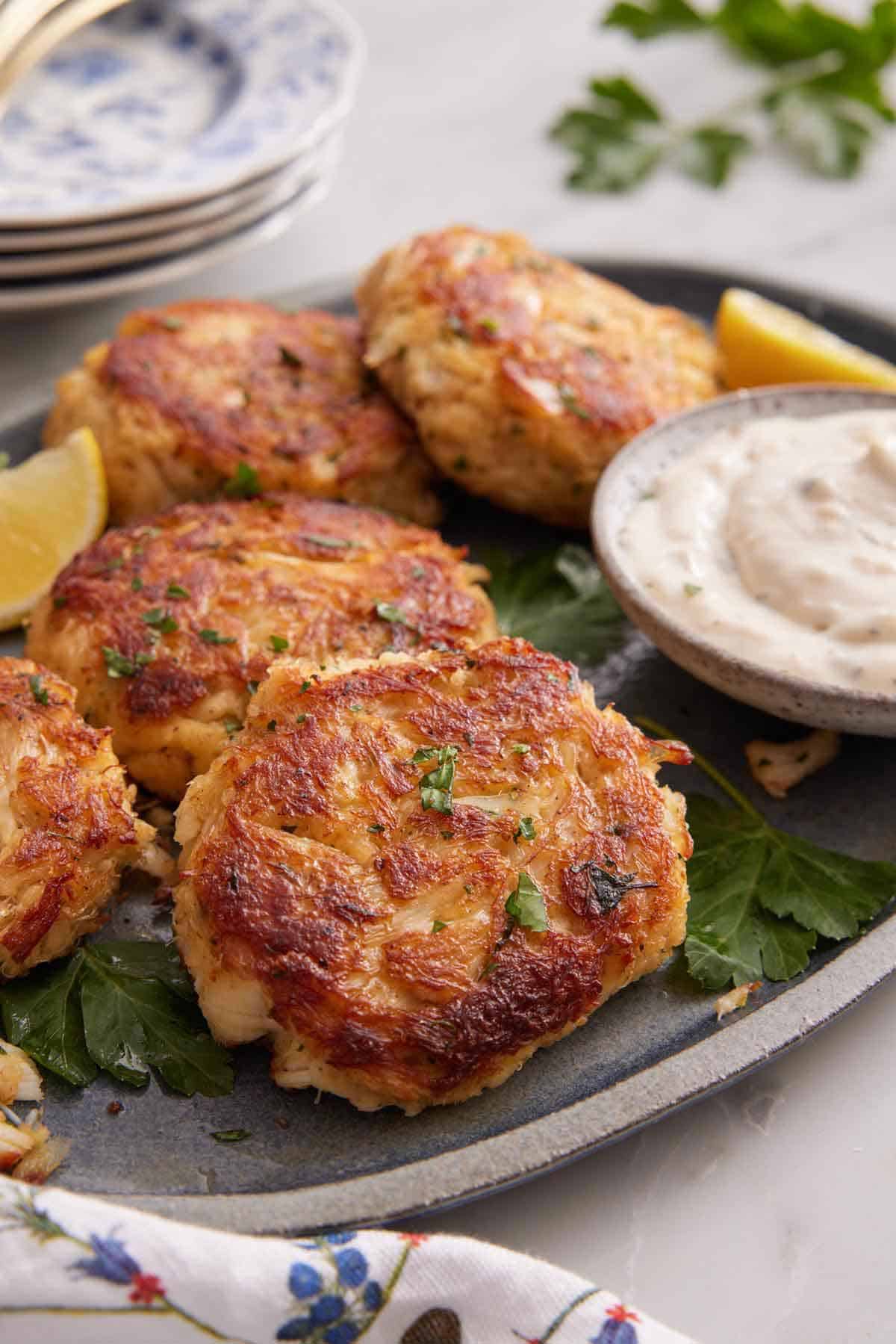 A platter of crab cakes with parsley, lemon wedges, and tartar sauce.