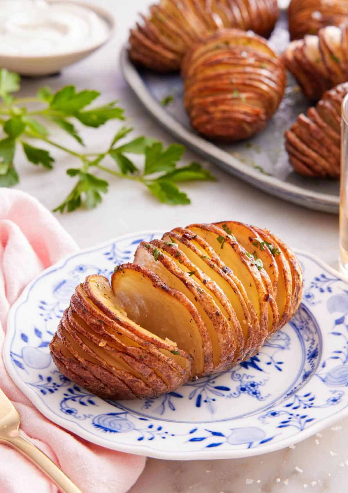 A plate with a hasselback potato with more on a platter in the background.