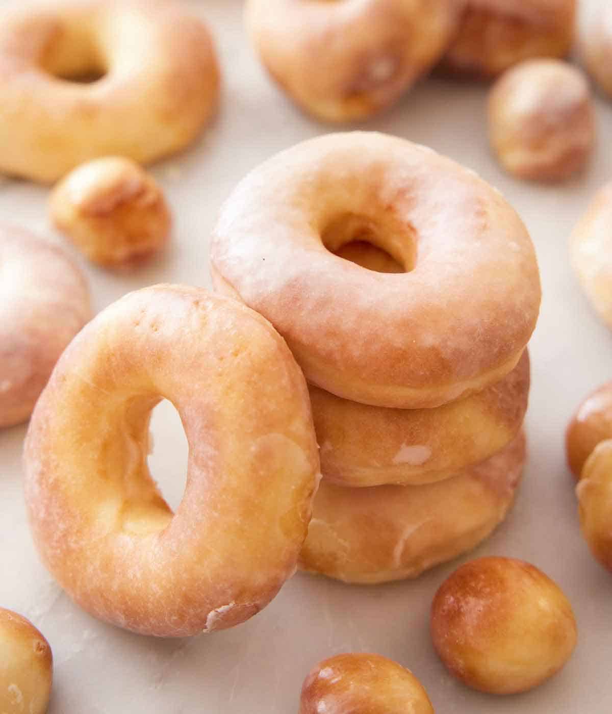 A stack of three air fryer donuts with another leaned on it and more donuts and donut holes scattered.