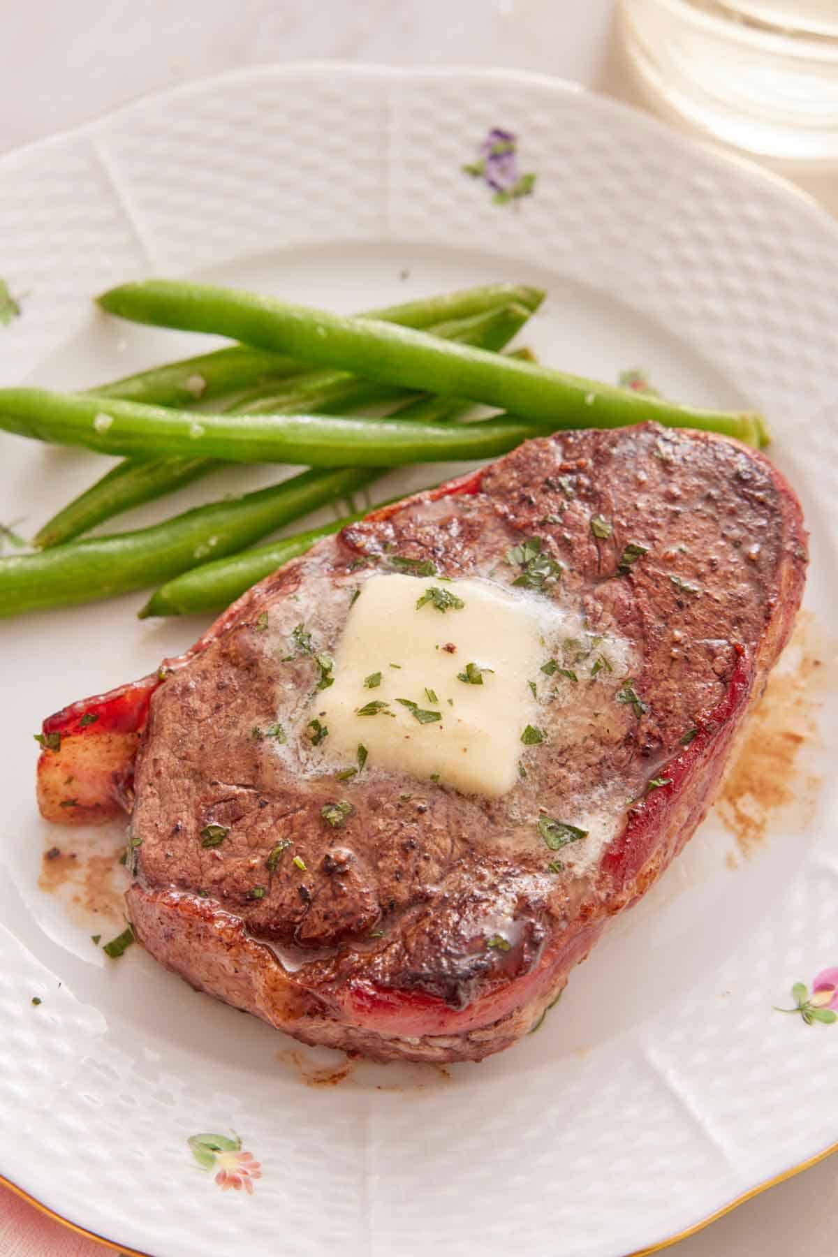 A plate with a bacon wrapped filet mignon with a pat of melted butter on top with some green beans on the side.