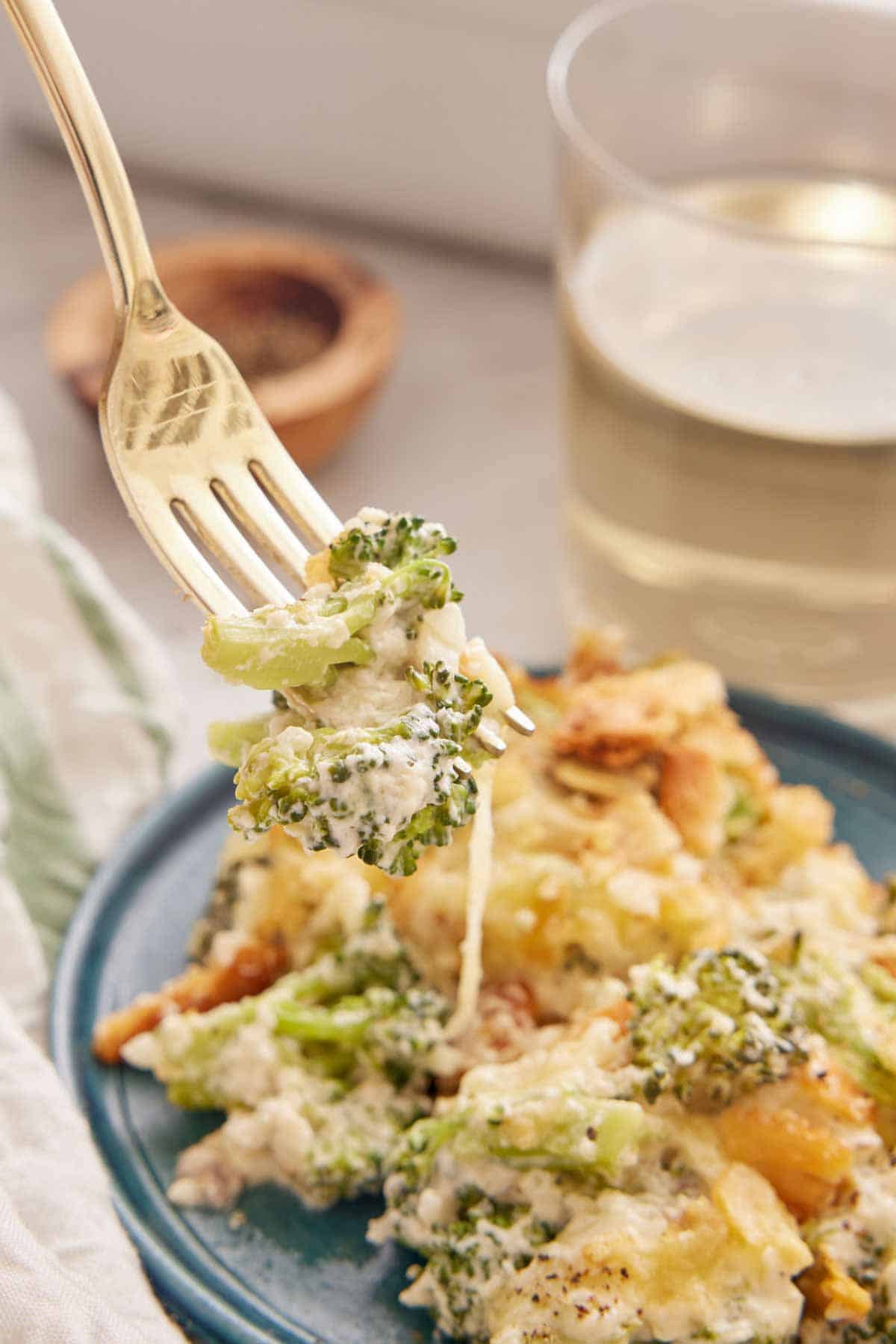 A forkful of broccoli casserole lifted from a plate with a glass of wine in the background.