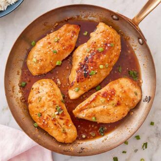 Overhead view of a skillet with four honey garlic chicken with green onions and sesame seeds on top.