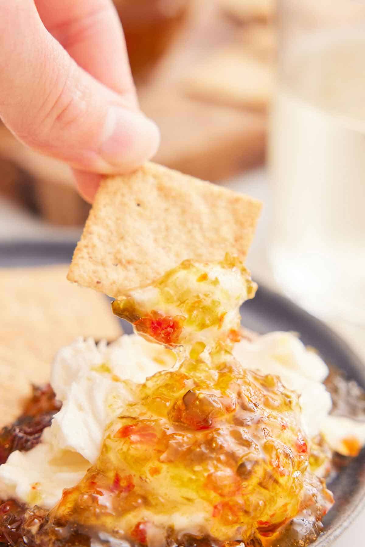 A cracker scooping up a bit of jalapeno jelly from a plate.