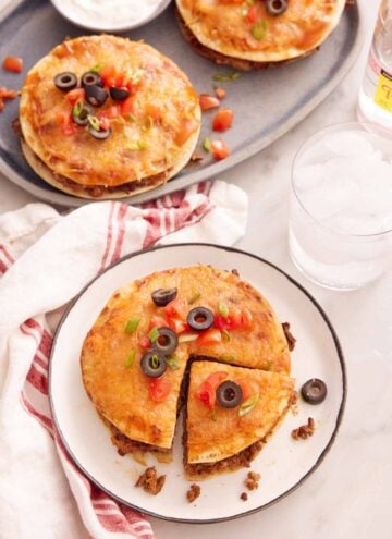 A plate with a Mexican pizza with a slice cut with a platter in the back with two more.