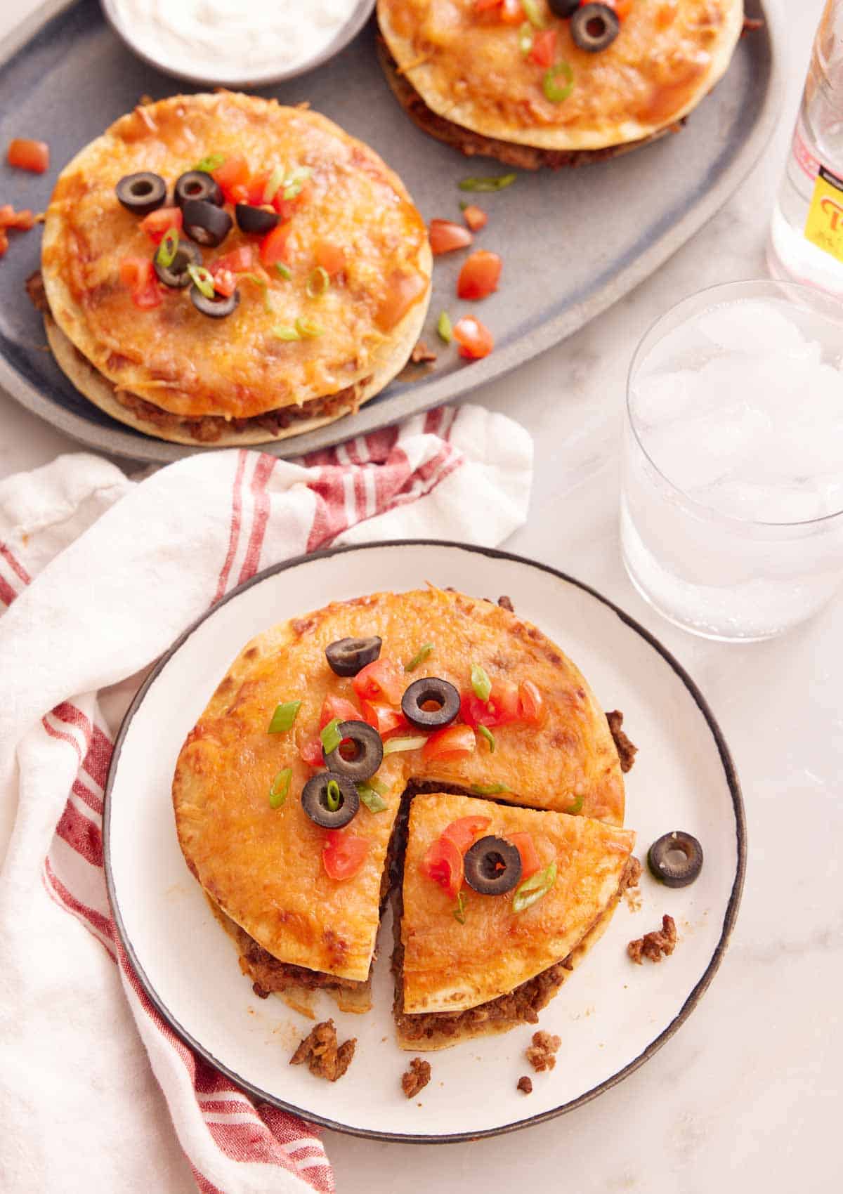 A plate with a Mexican pizza with a slice cut with a platter in the back with two more.