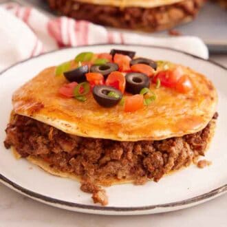 A plate with a Mexican pizza topped with chopped olives, tomatoes, and green onions.