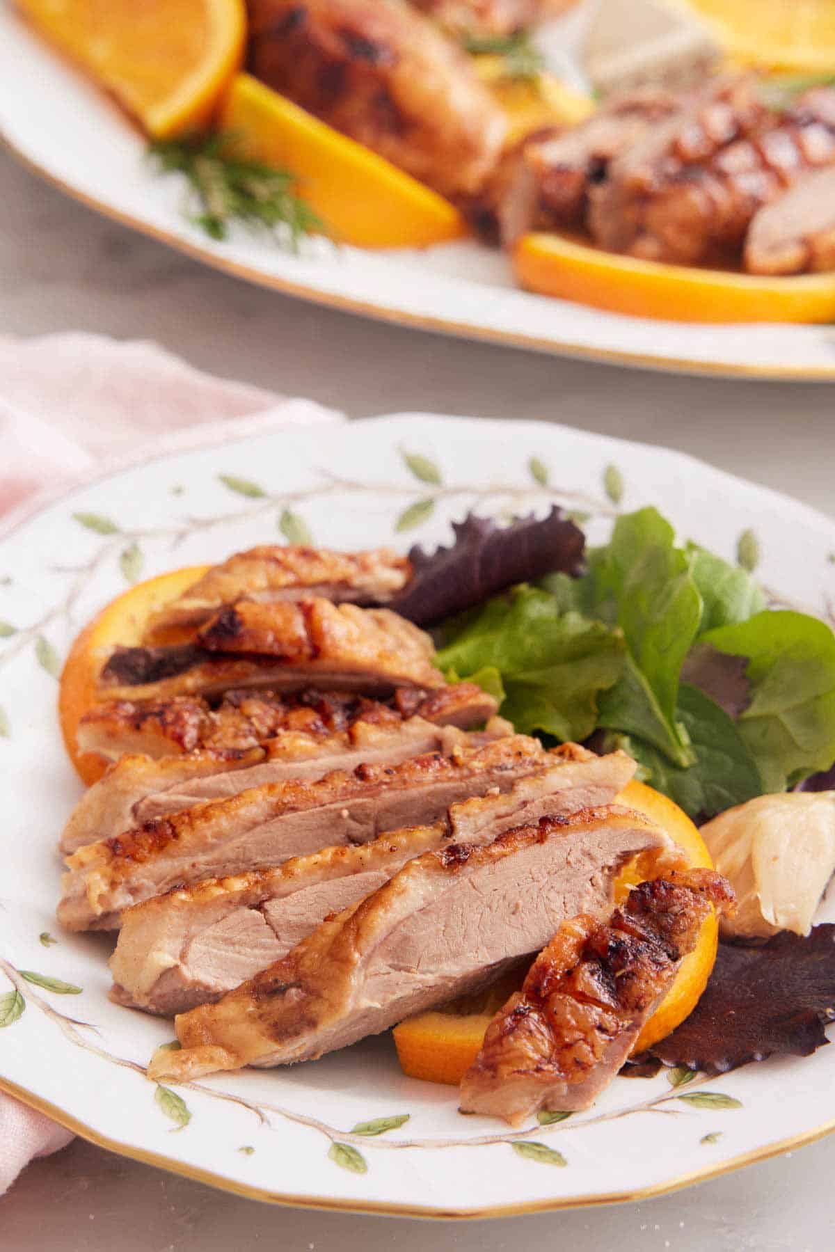 A plate with a sliced serving of roasted duck with some greens.