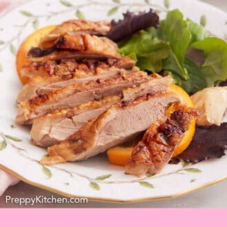 Pinterest graphic of a plate with sliced roasted duck with some greens and orange slices.