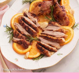 Pinterest graphic of sliced and plated roasted duck on a platter over orange slices.