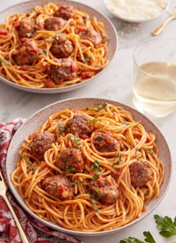 Two plates of spaghetti and meatballs with a glass of wine inbetween.