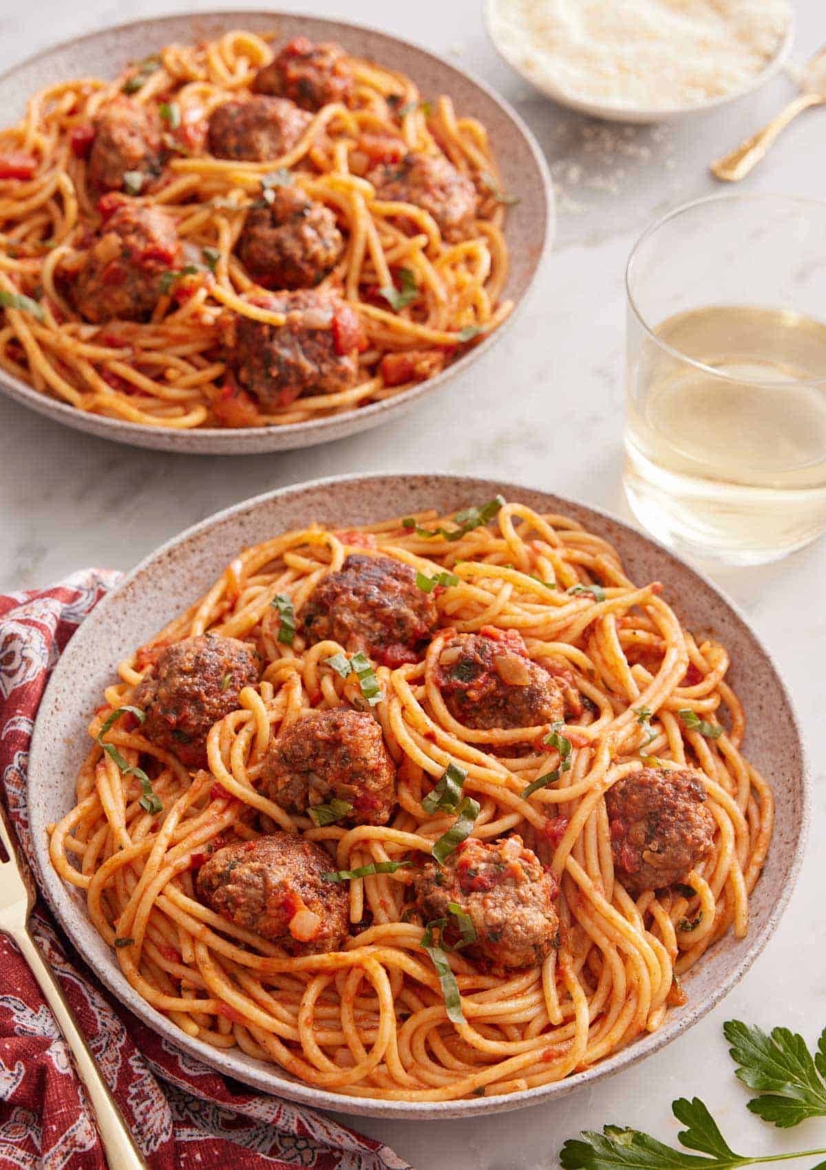 Two plates of spaghetti and meatballs with a glass of wine inbetween.