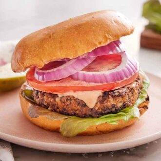 A plate with a veggie burger with a cut pickle in behind it.