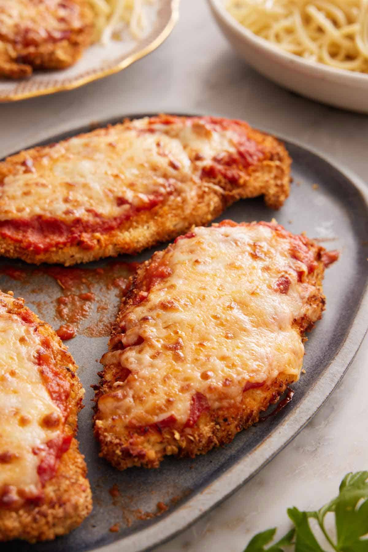 A platter showing three air fryer chicken parmesan with some noodles in a plate in the background.