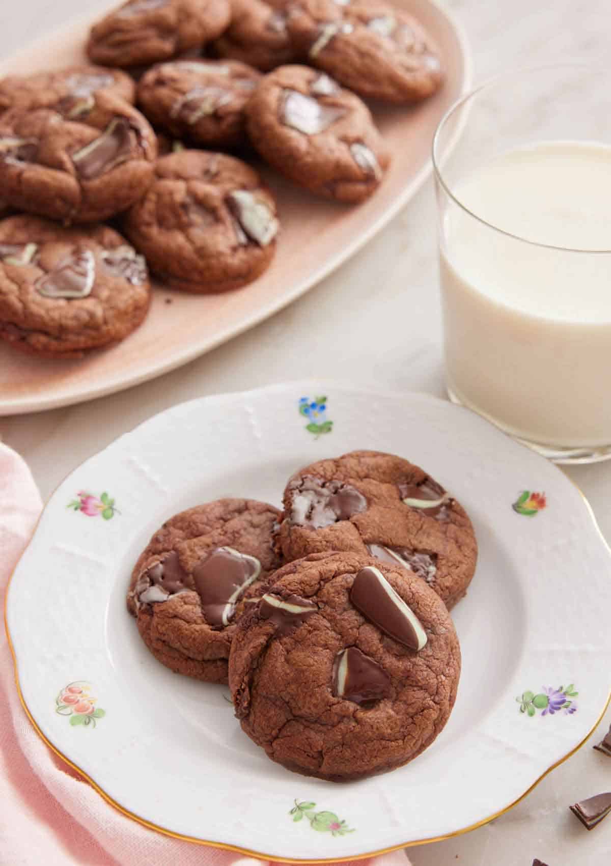 A plate with three Andes Mint Cookies with a glass of milk and platter of cookies in the background.