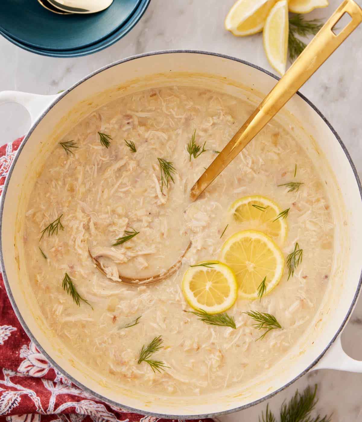 Overhead view of a pot of avgolemono garnished with dill and lemon slices. A ladle inside.