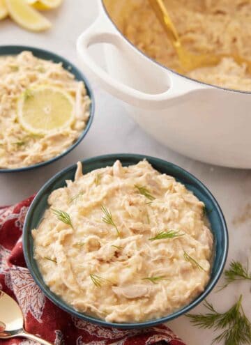 A bowl of avgolemono with a large pot and second bowl of avgolemono in the background.