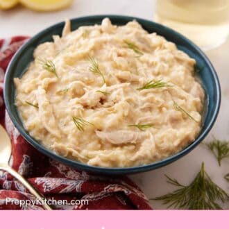 Pinterest graphic of a blue bowl of avgolemono with a drink in the background along with lemon wedges.