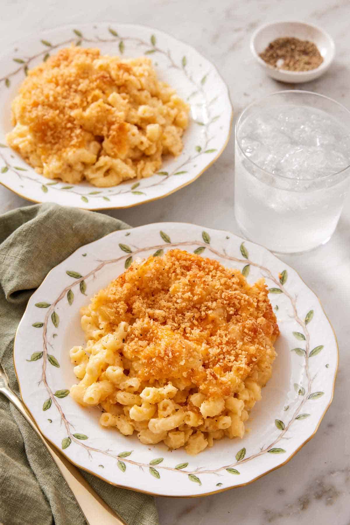 Two plates of baked mac and cheese with a glass of water in between.