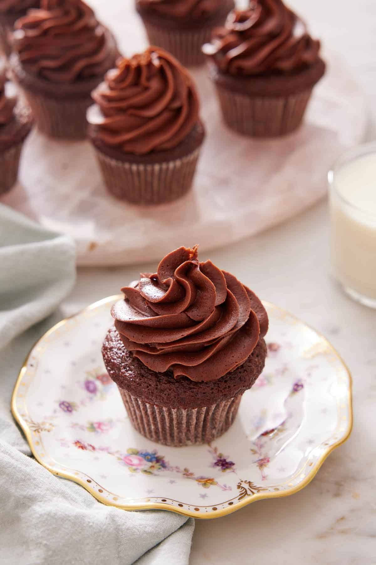 A chocolate cupcake on a plate with more on a platter in the background.