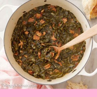 Pinterest graphic of overhead view of a pot of collard greens with a wooden spoon inside. Torn bread off to the side.