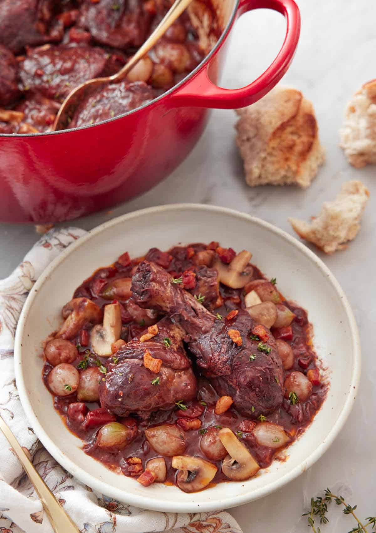 A plate of coq au vin with torn bread and a large pot in the background.