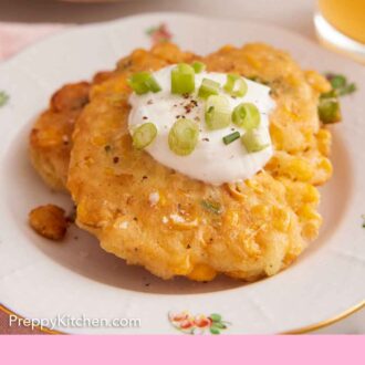 Pinterest graphic of two corn fritters topped with a dollop of sauce topped with green onions.