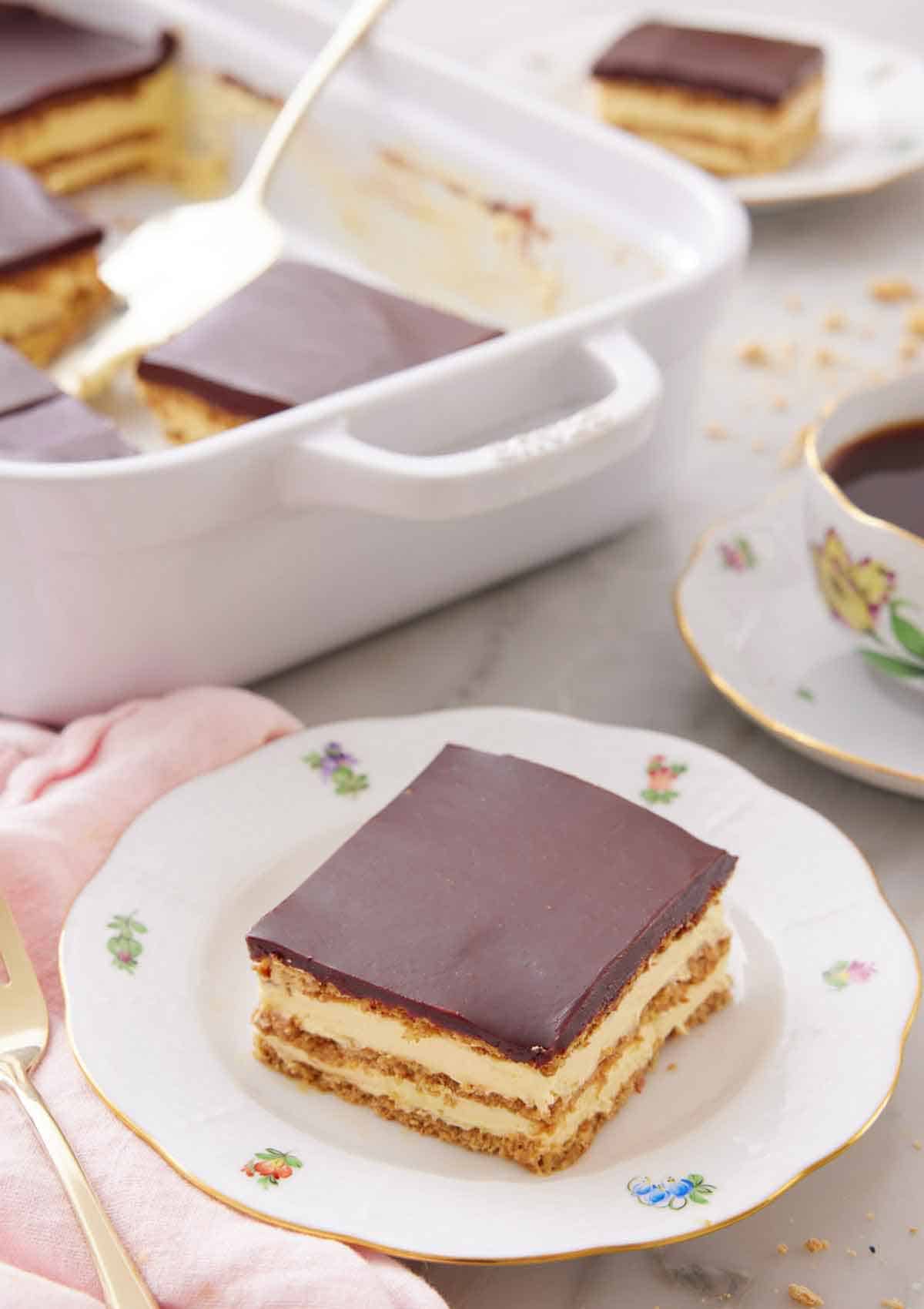 A plate with a slice of éclair cake with a baking dish in the background.