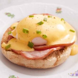 A close up view of eggs benedict on a plate with hollandaise sauce and chives on top.