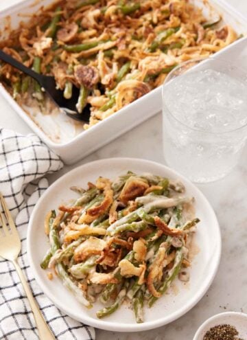 A plate with a serving of green bean casserole with a glass of water and baking dish in the background.