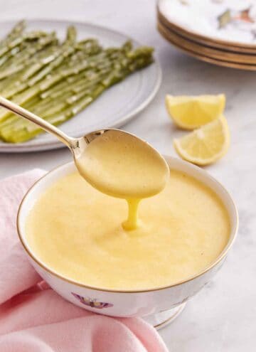A bowl of hollandaise sauce with a spoonful lifted up with the sauce drizzling off.