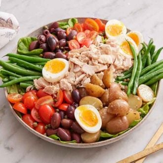 A platter of niçoise salad. Serving spoons and a linen napkin on the side.