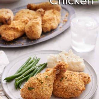 Pinterest graphic of a plate of oven fried chicken with green beans and mashed potatoes. A glass of water and platters of food in the background.