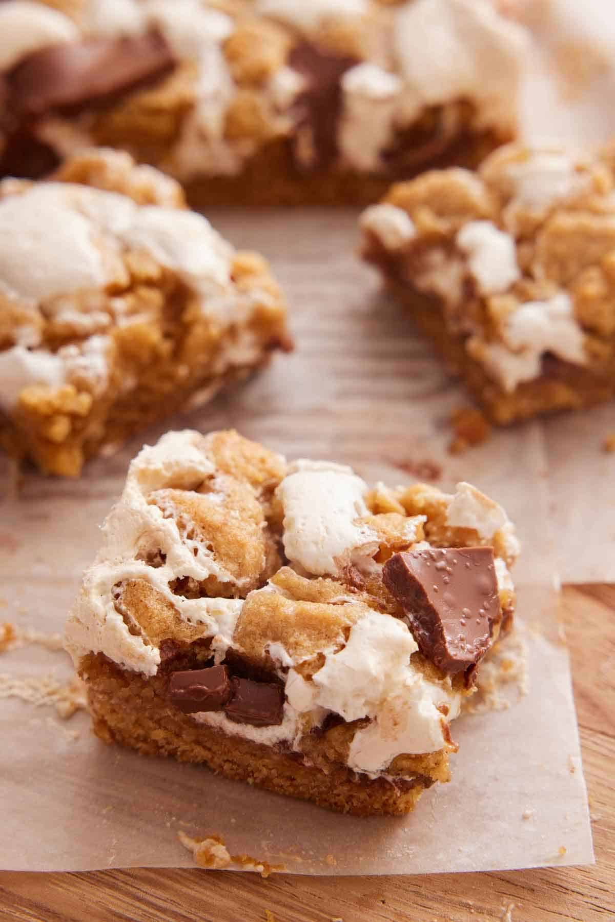 A wooden serving board lined with parchment with a slice of s'mores bar in focus with more in the back.