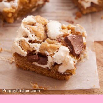 Pinterest graphic of a wooden serving board lined with parchment with a slice of s'mores bar in focus with more in the back.
