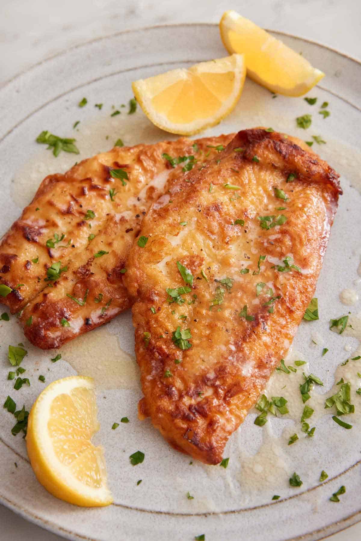 A plate with sole meunière with lemon wedges and parsley as garnish.