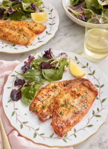 Two plates of sole meunière with a handful of mixed greens and a lemon wedge.