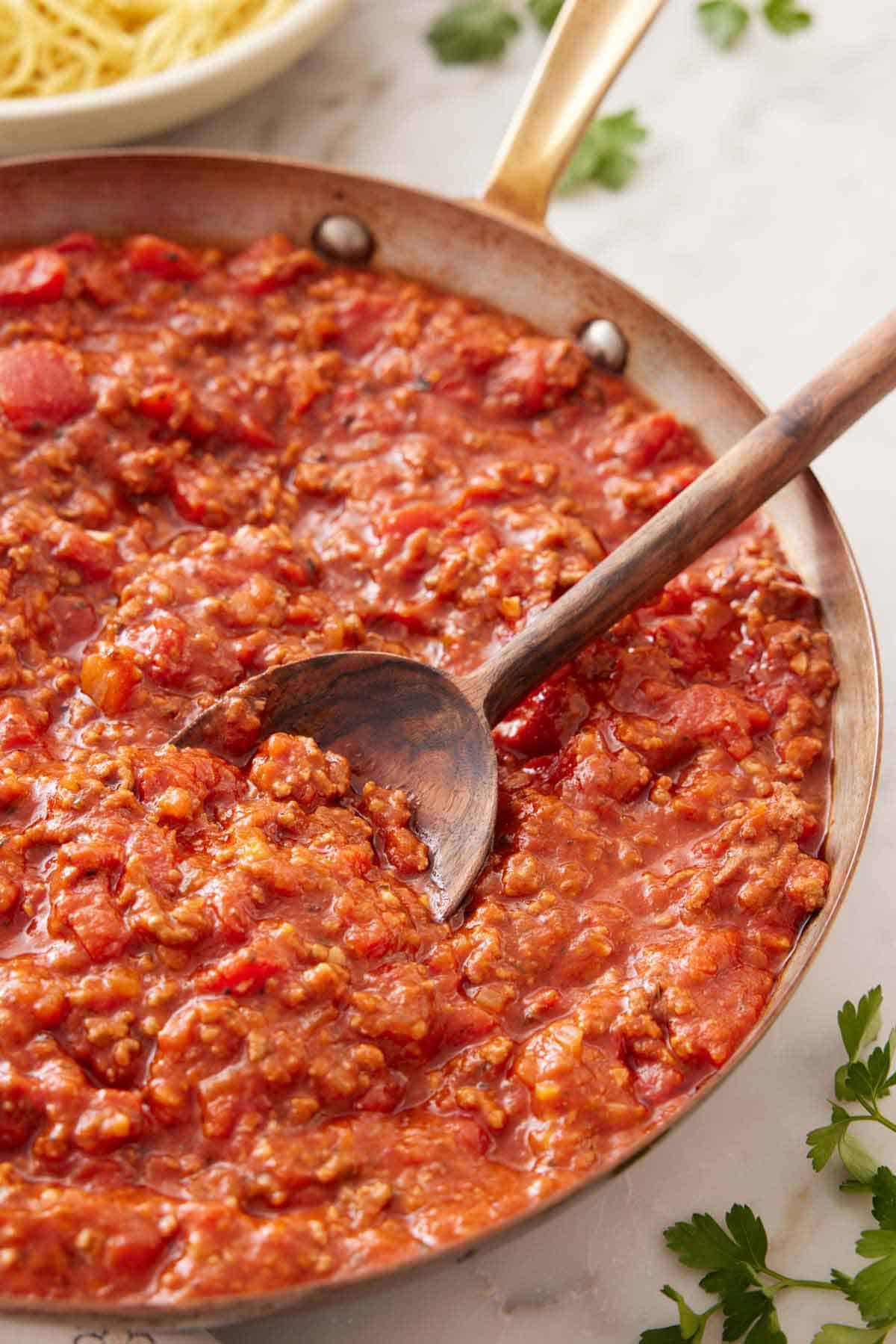 A skillet of spaghetti sauce with a large serving spoon tucked in.