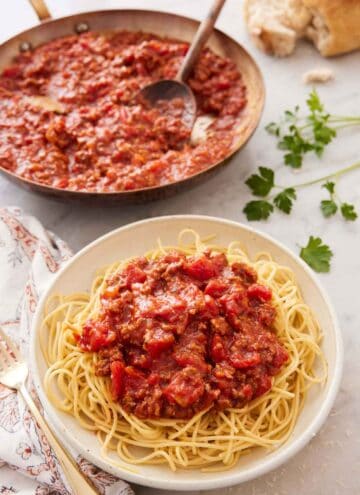 A bowl of noodles with spaghetti sauce on top with a skillet full of sauce in the background.