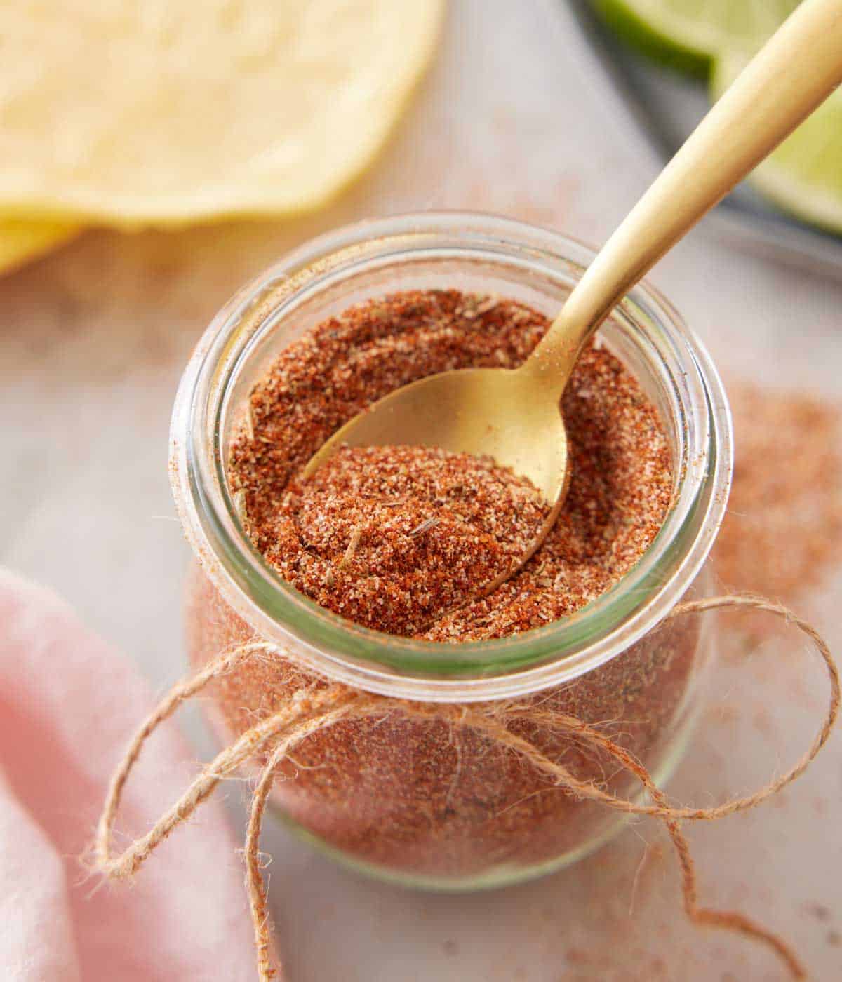 Overhead view of a spoon scooping out taco seasoning from a jar.
