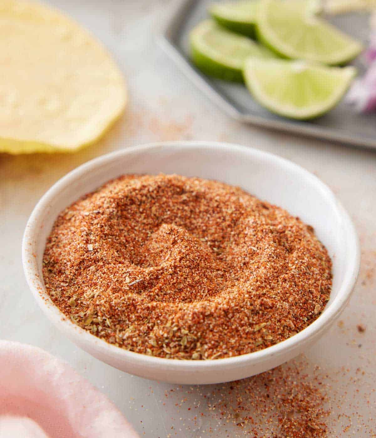 A small plate filled with taco seasoning with some taco ingredients in the background.