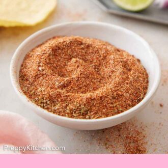 Pinterest graphic of a small plate filled with taco seasoning with some taco ingredients in the background.