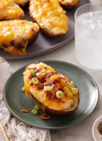 A plate with a twice-baked potato topped with green onions with a platter with more in the background.