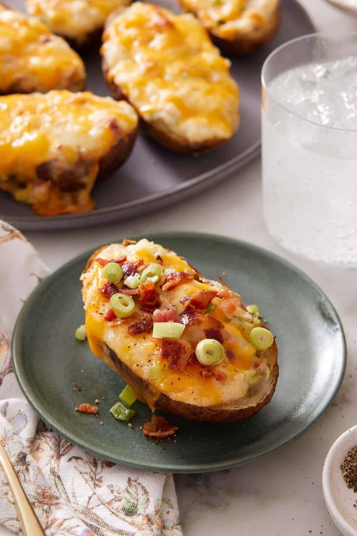 A plate with a twice-baked potato topped with green onions with a platter with more in the background.