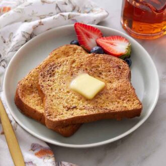 A plate with two pieces of air fryer french toast with butter on top and berries off to the side.