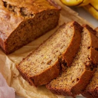 Four slices of banana bread in front of the rest of the loaf on brown parchment paper.
