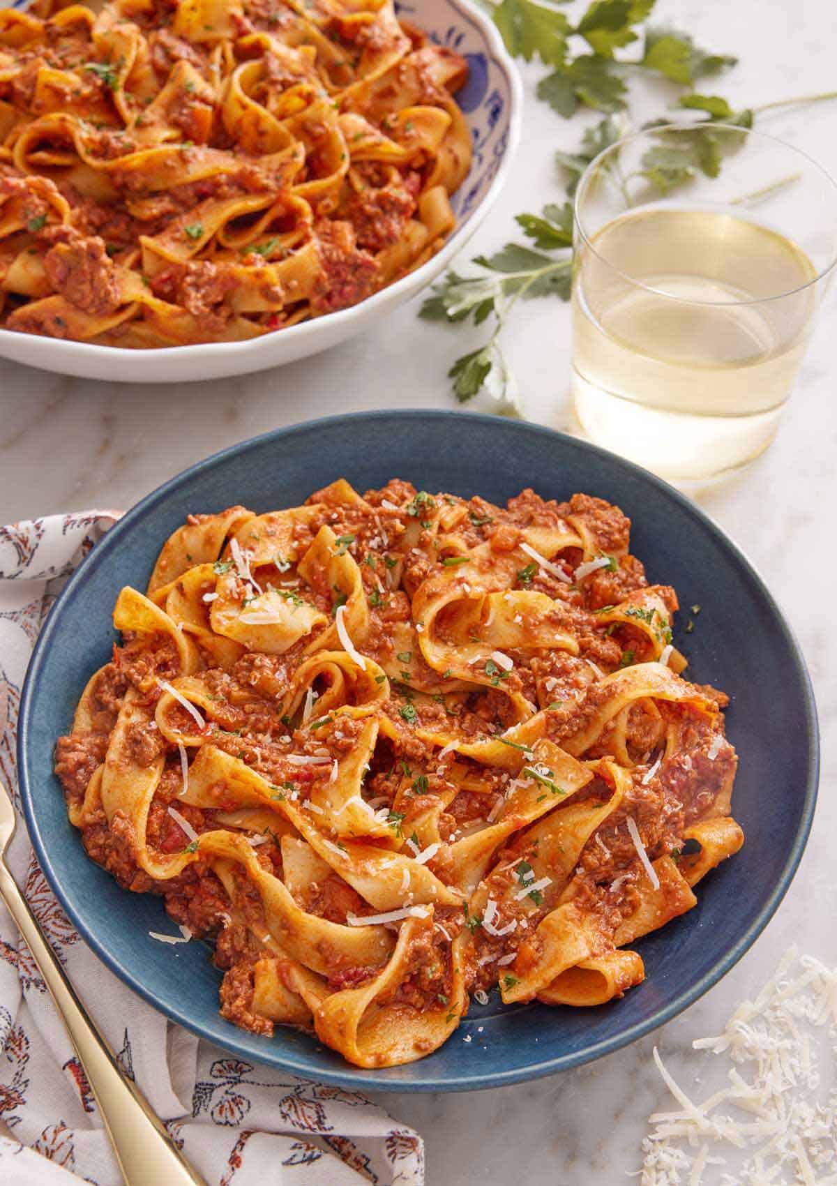 A bowl of bolognese with a glass of wine and a second bowl in the background.