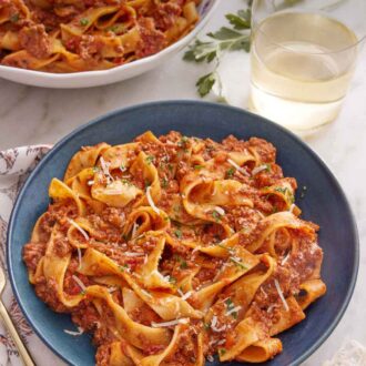 Pinterest graphic of a bowl of bolognese with a glass of wine and a second bowl in the background.