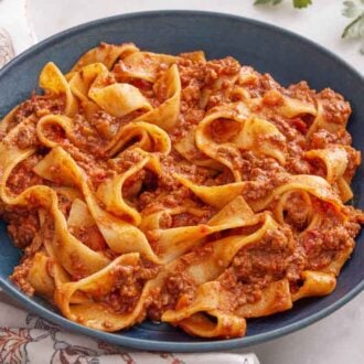 A bowl of bolognese with utensils on the side and parsley.