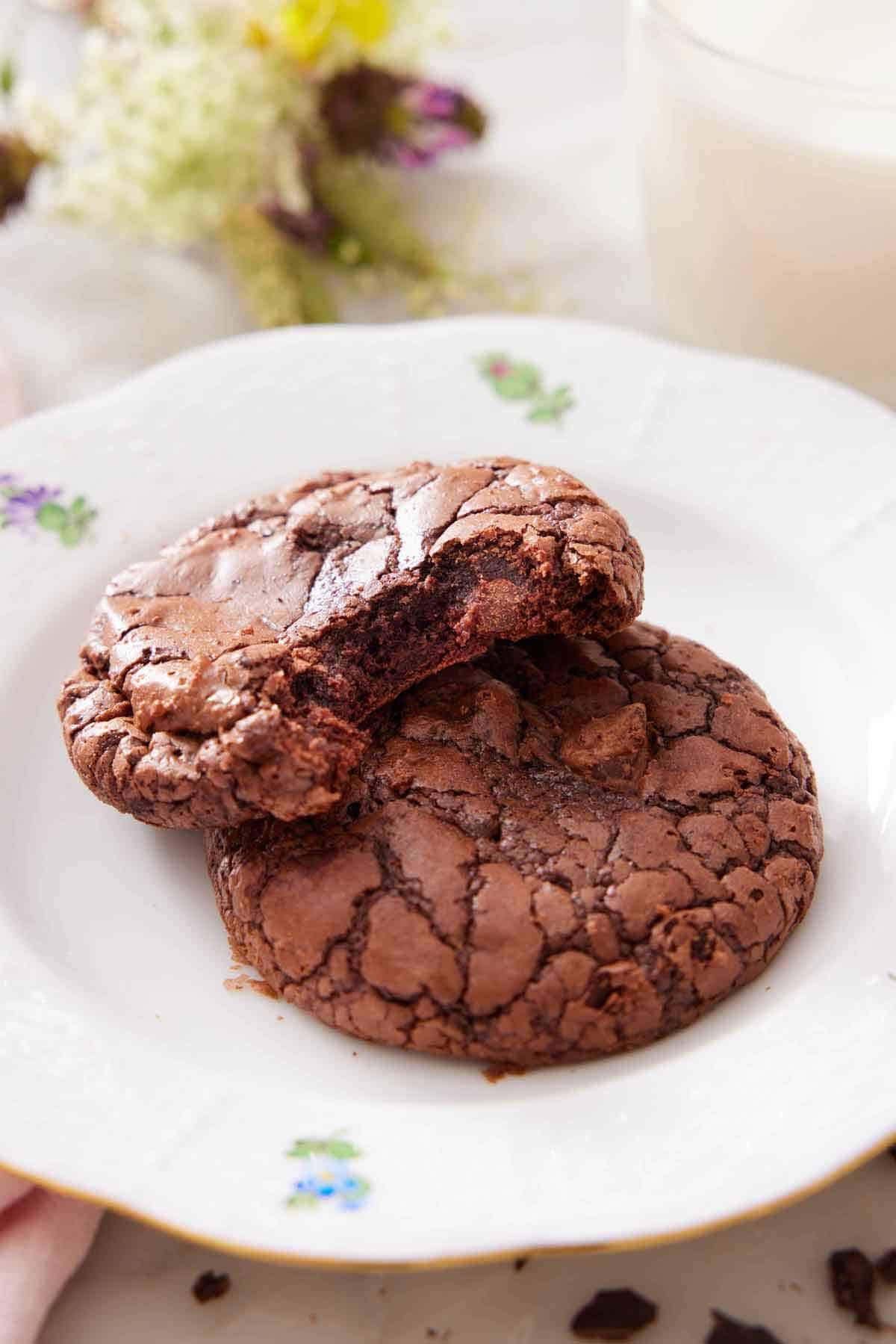 A plate with two brownie cookies, one with a bite taking out of it.