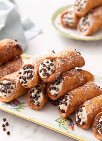 A platter with a stack of cannoli with a plate of three more in the background.